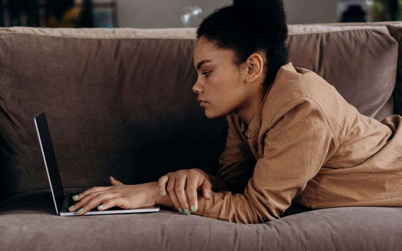 en kvinna ligger i soffa och använder en laptop