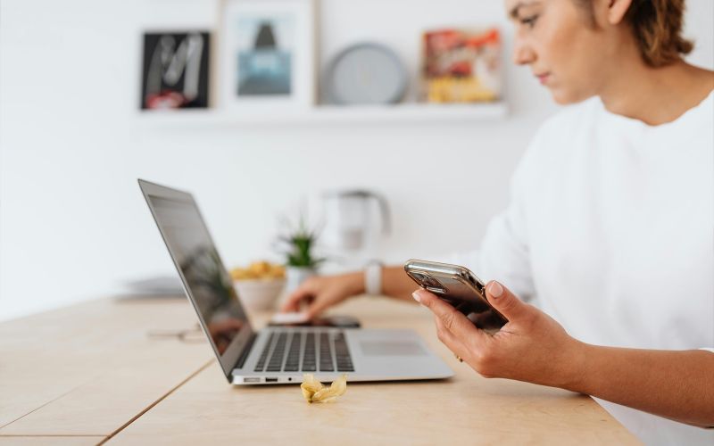 en kvinna sitter med laptop och smartphone